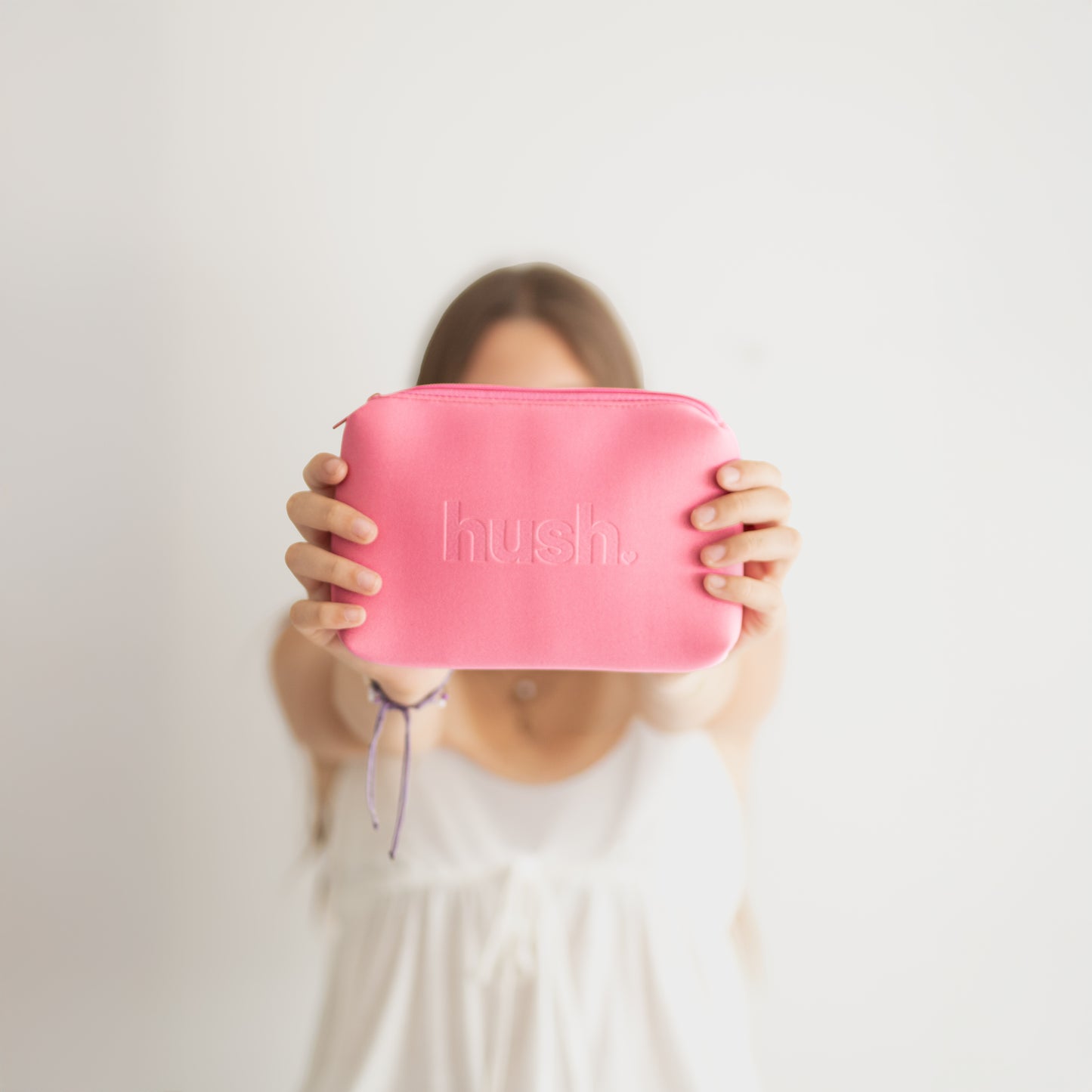 Person holding a pink pouch with 'hush' branding against a plain background