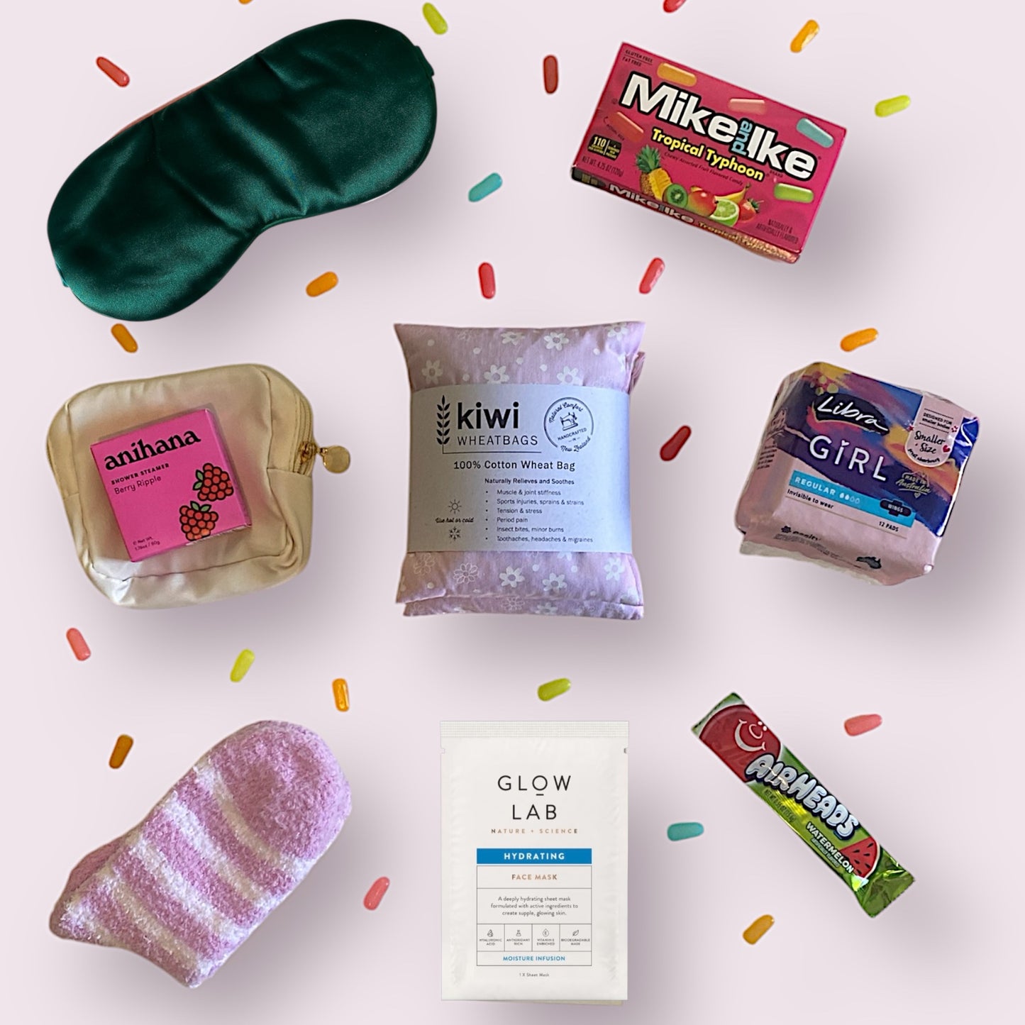 Items of gift box on display. Eye mask, Mike and Ike american candy, little purse, anihana shower steamer, kiwi wheatbag, libra teen pads, fluffy socks, glow lab face mask and airheads candy bar.