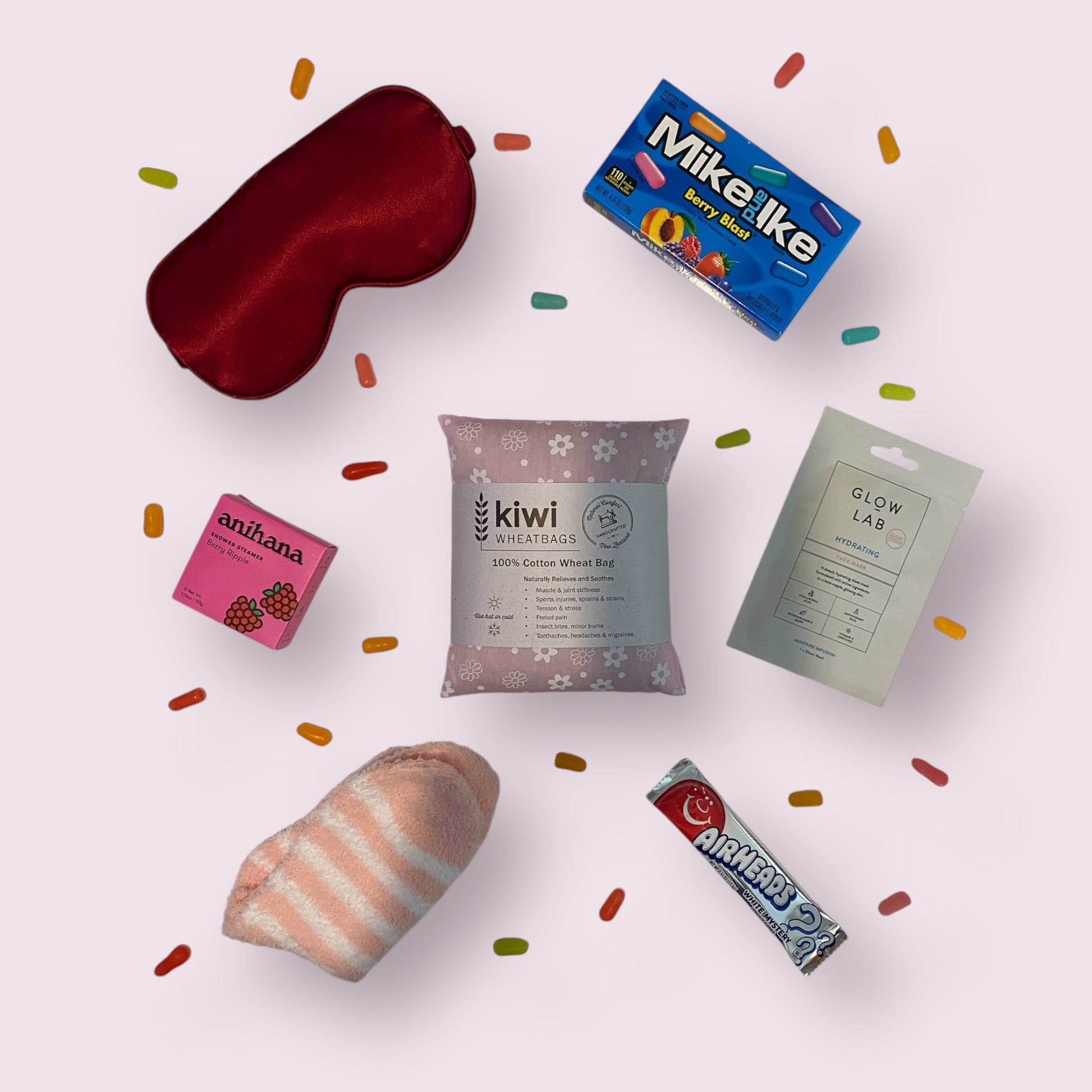 Contents of self care box including, silk eye mask, american candy, anihana shower steamer, kiwi wheatbag, glow lab face mask and fluffy socks.