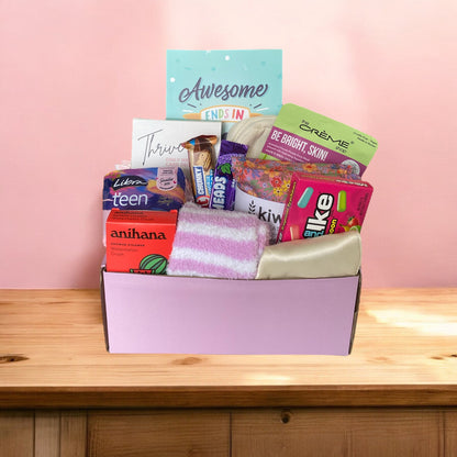 Items of gift box on disply in gift box. Awesome ends in me journal, american candy, thrive wellness cards, kiwi wheatbags, glow lab face mask, kit kat, airheads, eye mask, libra teen pads, fluffy socks and anihana shower steamer.
