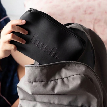 Black pouch with hush logo embossed on it being put into school bag