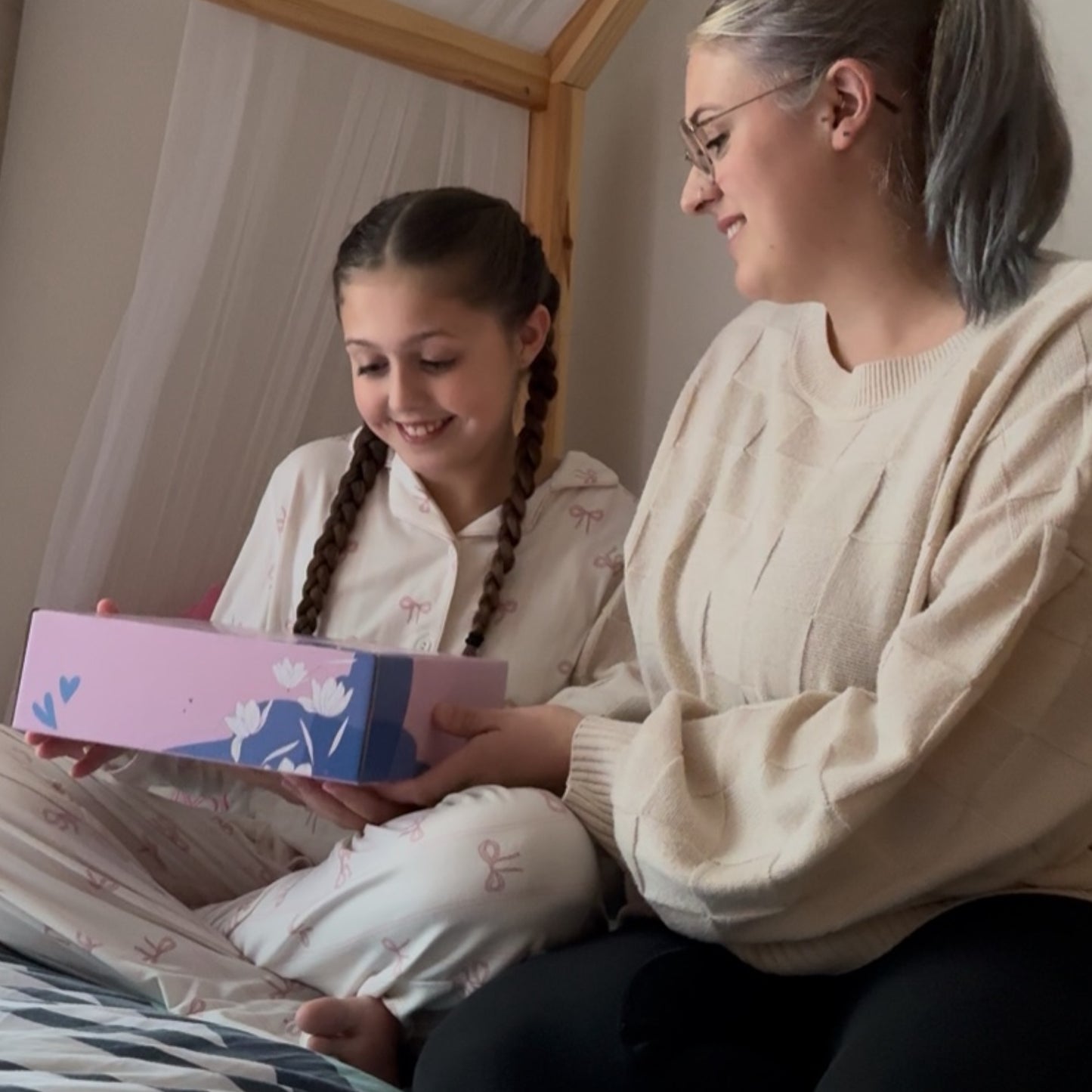Mum and Daughter sitting on bed about to open gift box.