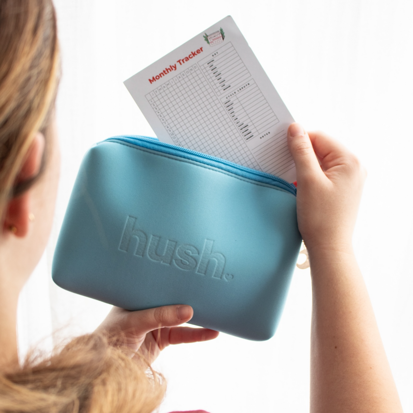 Person holding a blue 'hush' pouch with a 'Monthly Tracker' sheet