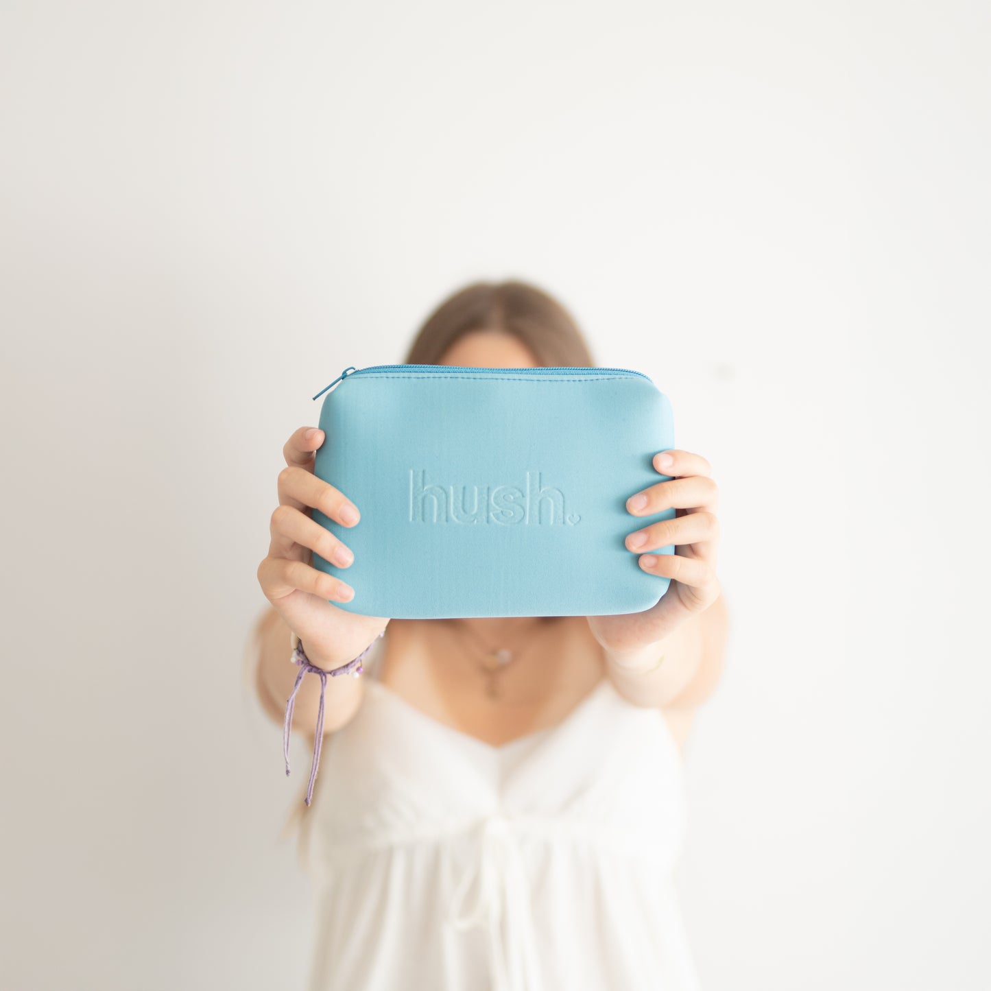 Person holding a blue pouch with 'hush' branding against a white background