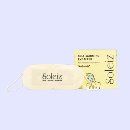 A cream-colored self-warming eye mask from Soleiz placed in front of its pale yellow packaging box, set against a solid light lavender background.