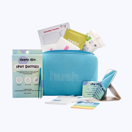 A blue pouch with the hush logo embossed on it. The pouch is filled with a monthly tracker, pads, wipes, little mirror, affirmation card and next to it s a packet of pimple pacthes.